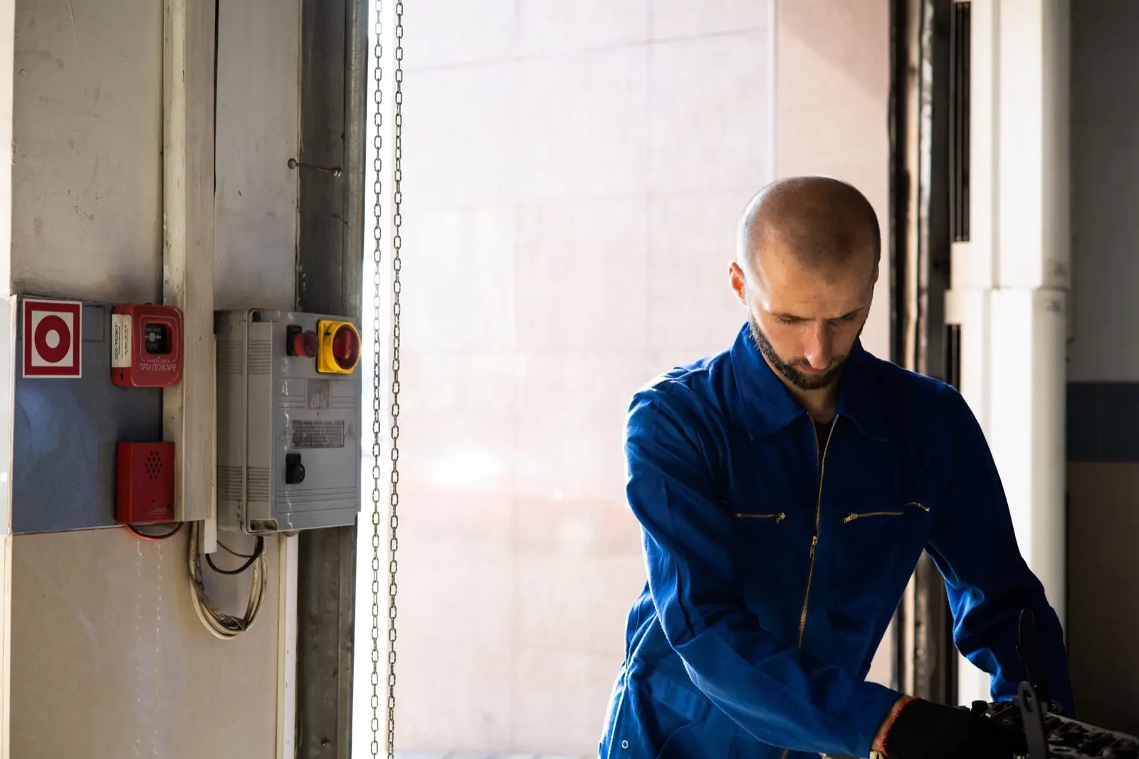 Elektriker in blauer Arbeitskleidung arbeitet an einer Anlage neben einem Schaltkasten