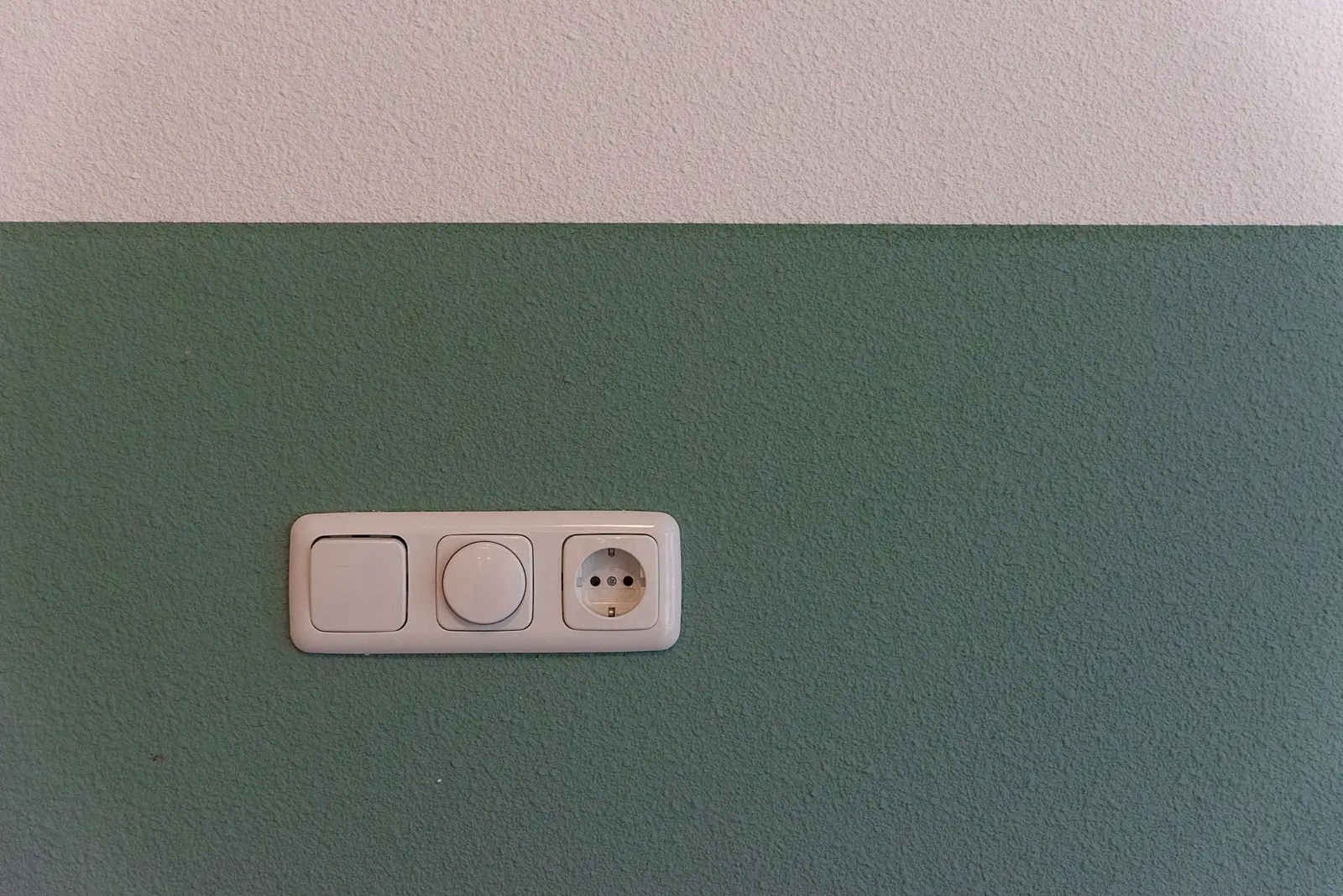 Neu montierte Schalter- und Steckdosenkombination an einer grün gestrichenen Wand