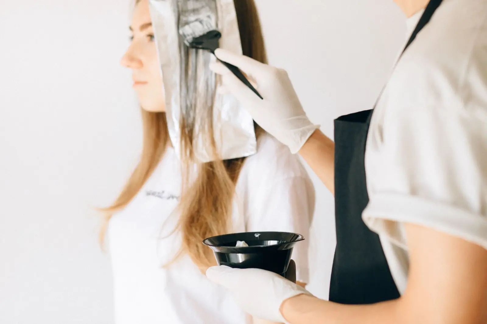 Friseurin trägt Farbe mit Pinsel auf Strähnen in Folie auf