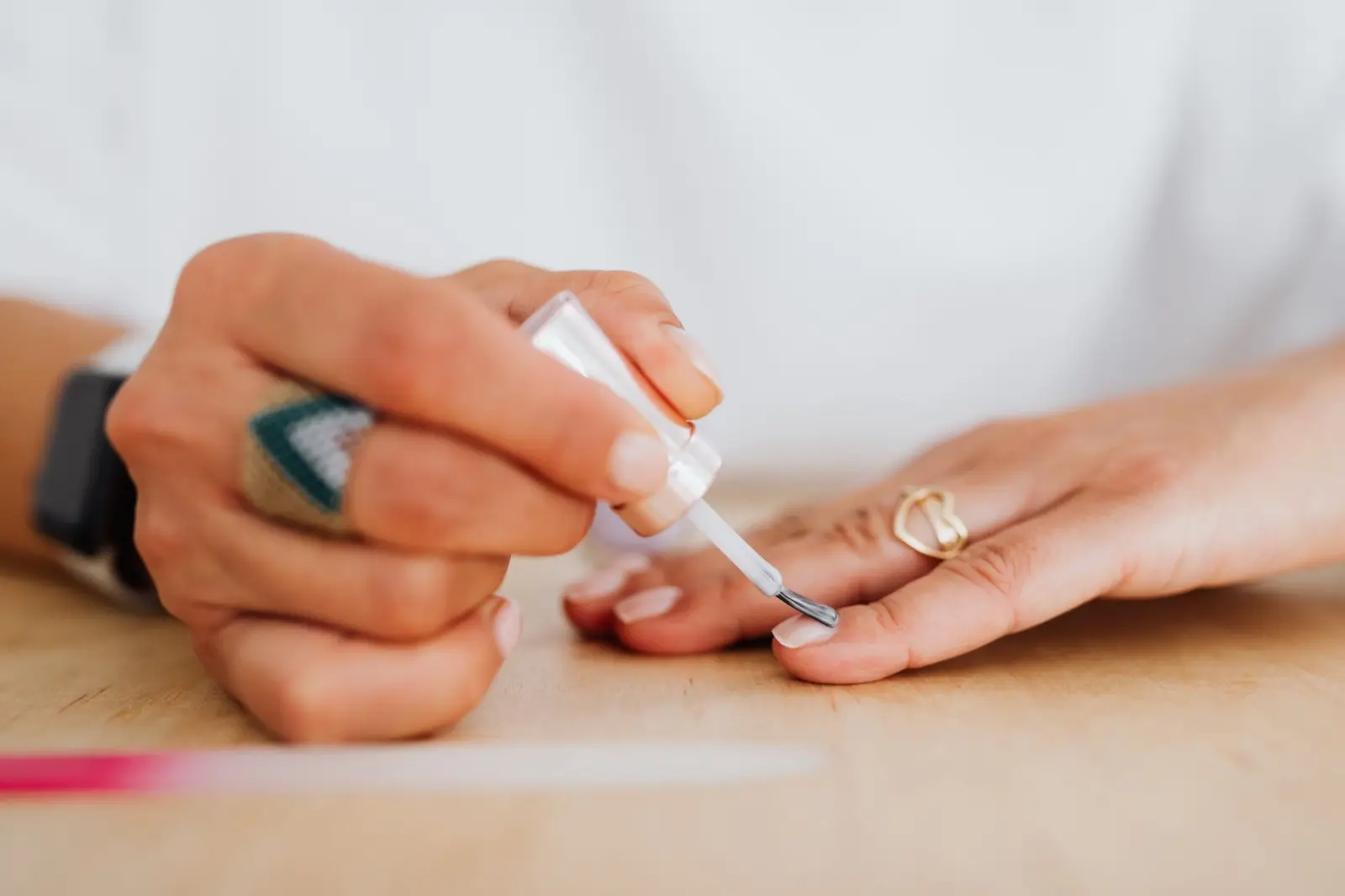 Hände bei der Maniküre an einem hellen Holztisch, Nagellack wird aufgetragen