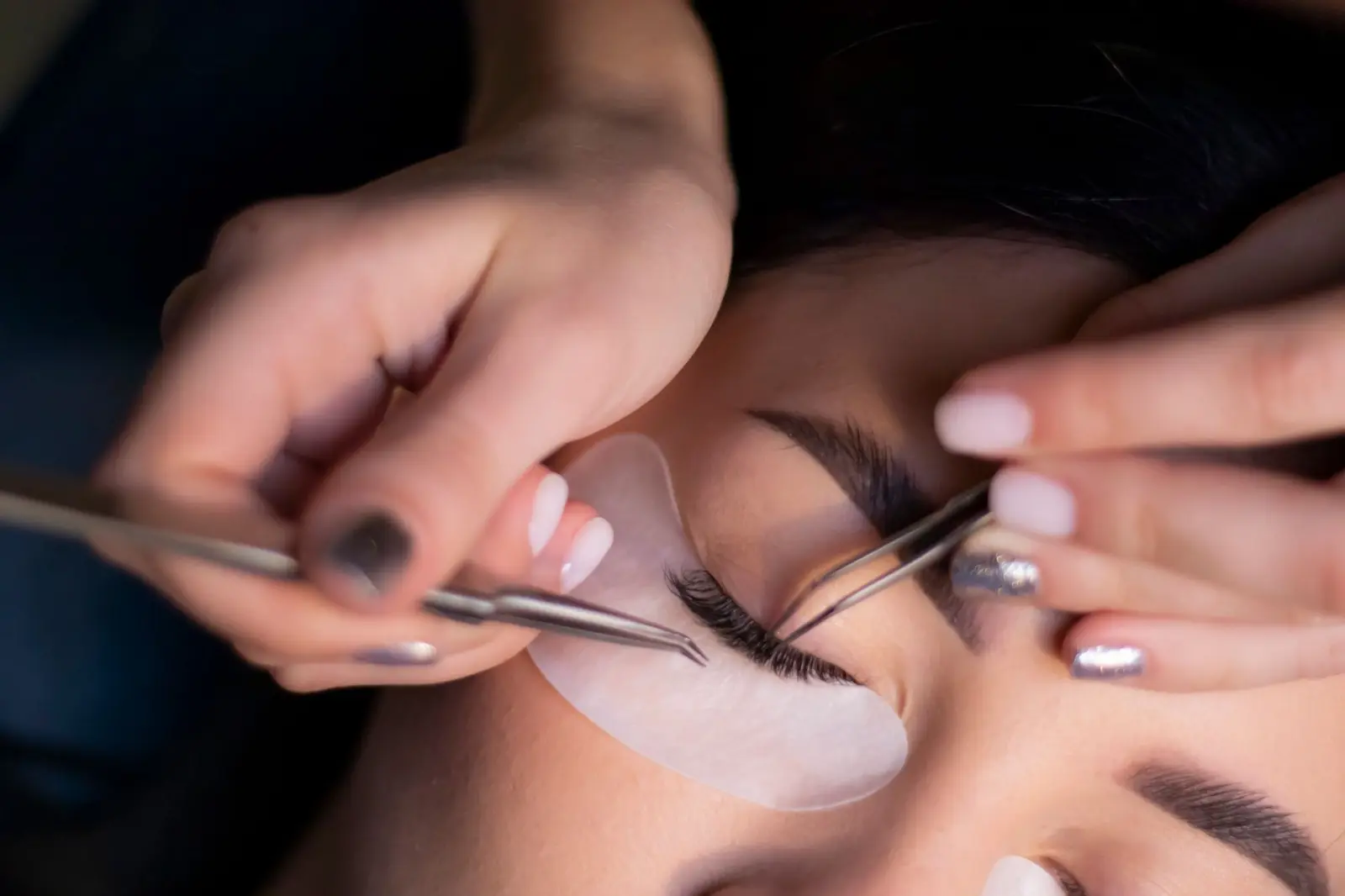 Nahaufnahme einer Wimpernbehandlung mit Augenpad und zwei Pinzetten