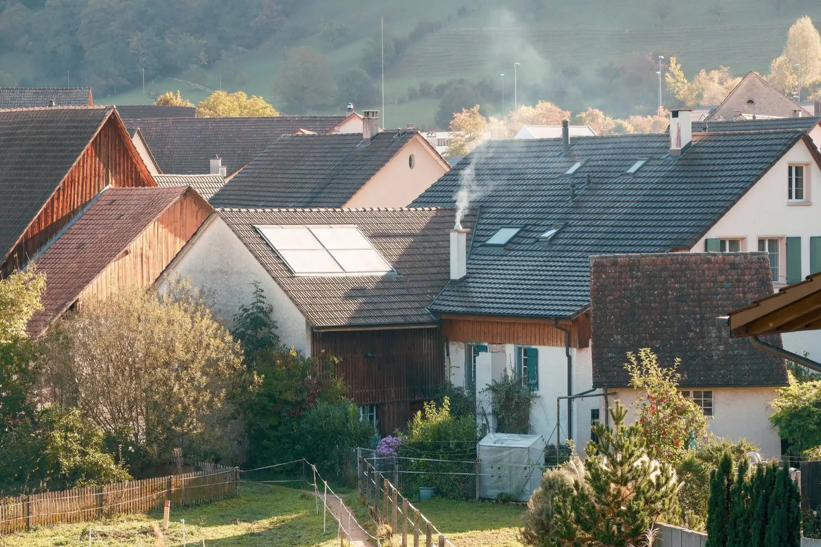 Dorf mit Holzhäusern im Herbst, aus einem Rauchfang steigt Rauch