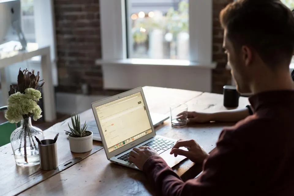 Ein Mann arbeitet an einem Holzschreibtisch mit Laptop, Pflanzen und Kaffeetasse in einem hellen Büro