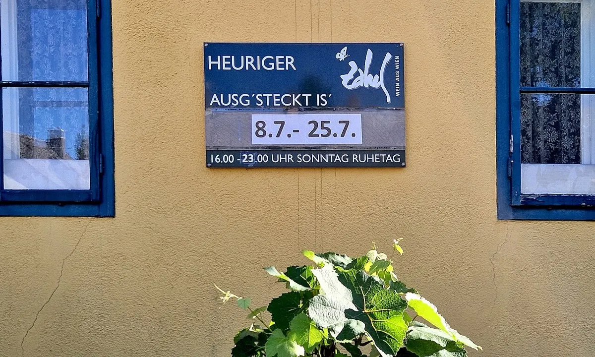 Schild an einer gelben Hauswand: Heuriger Zahel, ausg'steckt vom 8. Juli bis 25. Juli, mit Öffnungszeiten