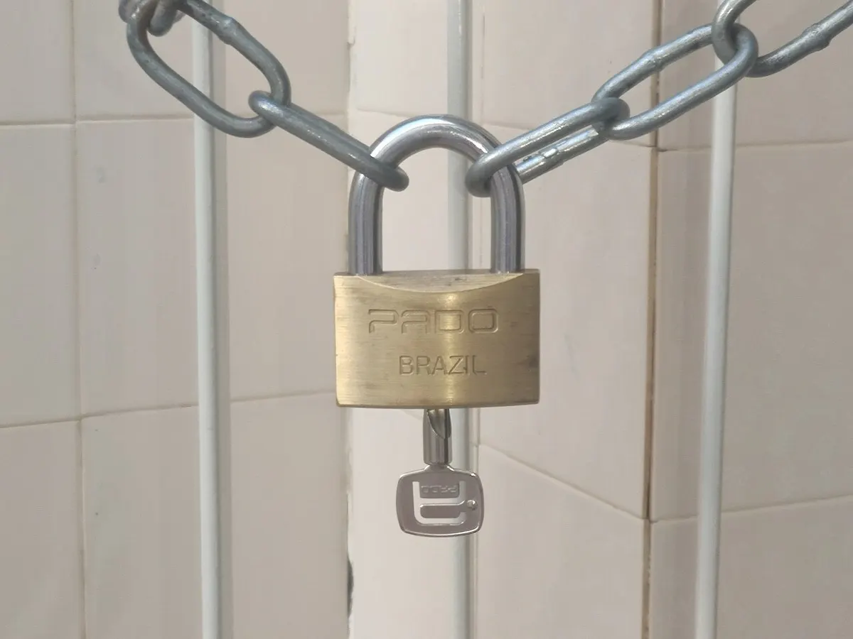 Ein Vorhängeschloss sichert eine Metallkette vor einer weiß gefliesten Wand